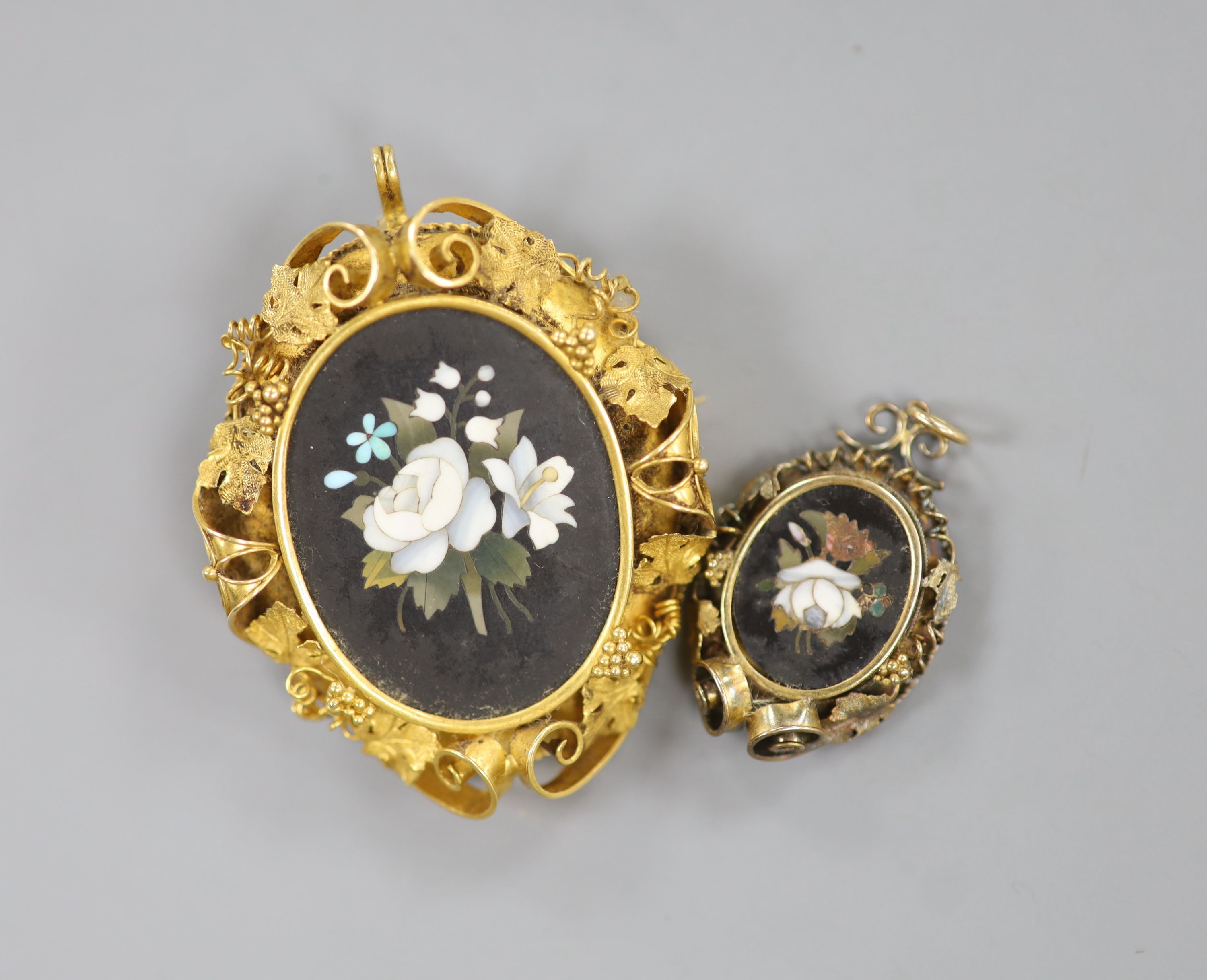 A Victorian yellow metal mounted pietra dura set oval pendant brooch, with fruiting vine border, 52mm, gross 21.3 grams and a similar gilt metal and pietra dura set pendant.